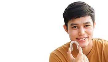 Teenage boy in orange shirt holding Invisalign