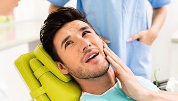 Man in dental chair holding cheek in pain