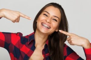 A woman with braces pointing to her smile