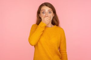 Shocked young woman with crowded teeth covering mouth