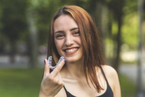 Smiling woman holding aligner during her Invisalign timeline