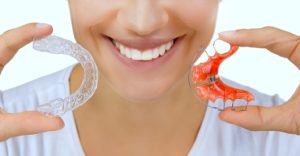 Woman holding a Hawley retainer and a clear plastic retainer