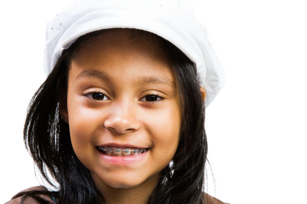 Smiling young girl in white hat with braces for children